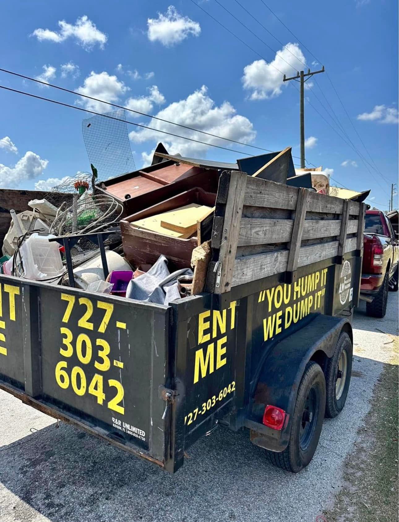 A dumpster trailer filled with junk is parked on the side of the road.