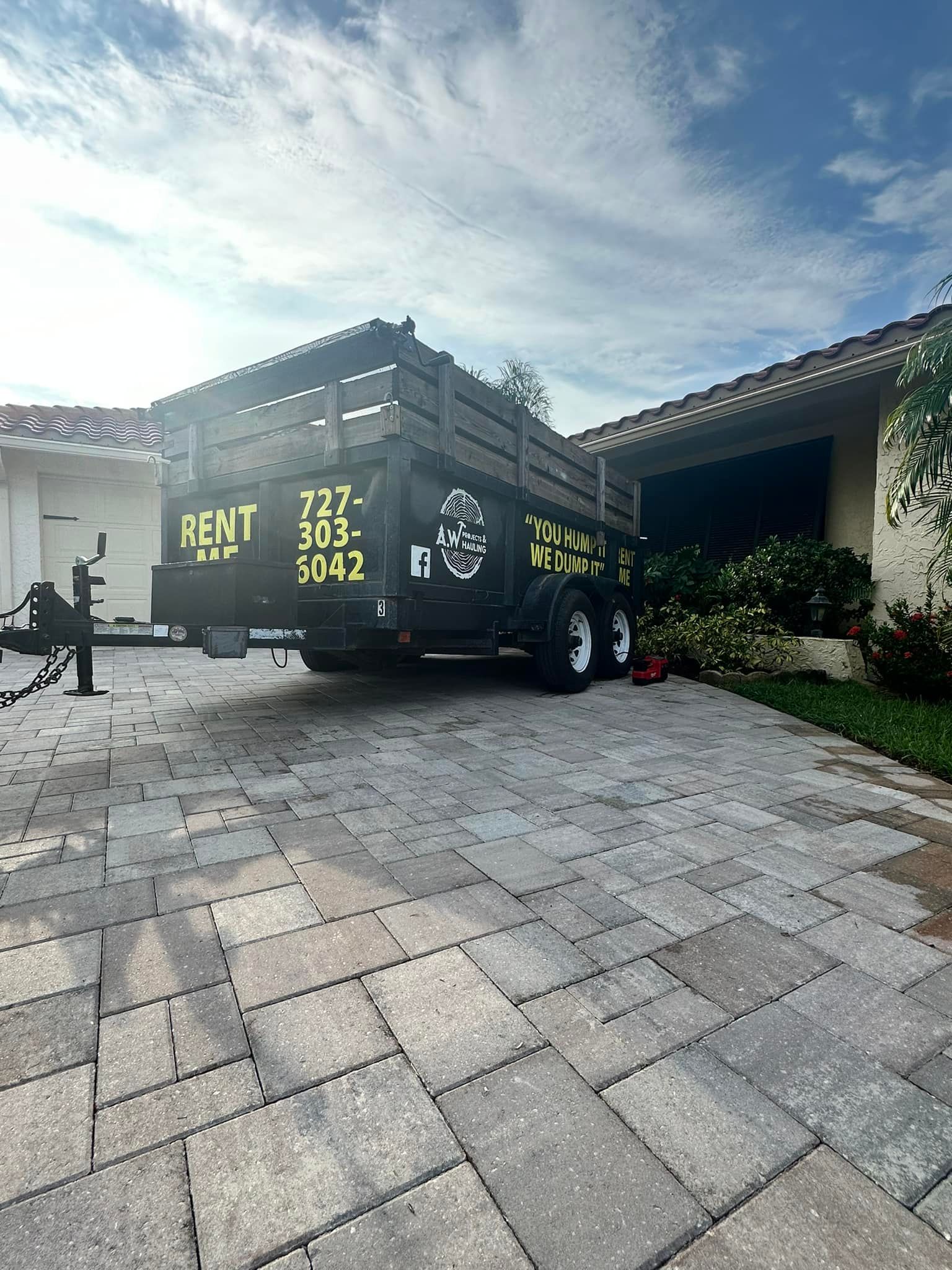 A trailer is parked in front of a house on a brick driveway.