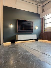 Dark green accent wall with TV, soundbar, floating cabinet, and sconces. Concrete floor with light strip.