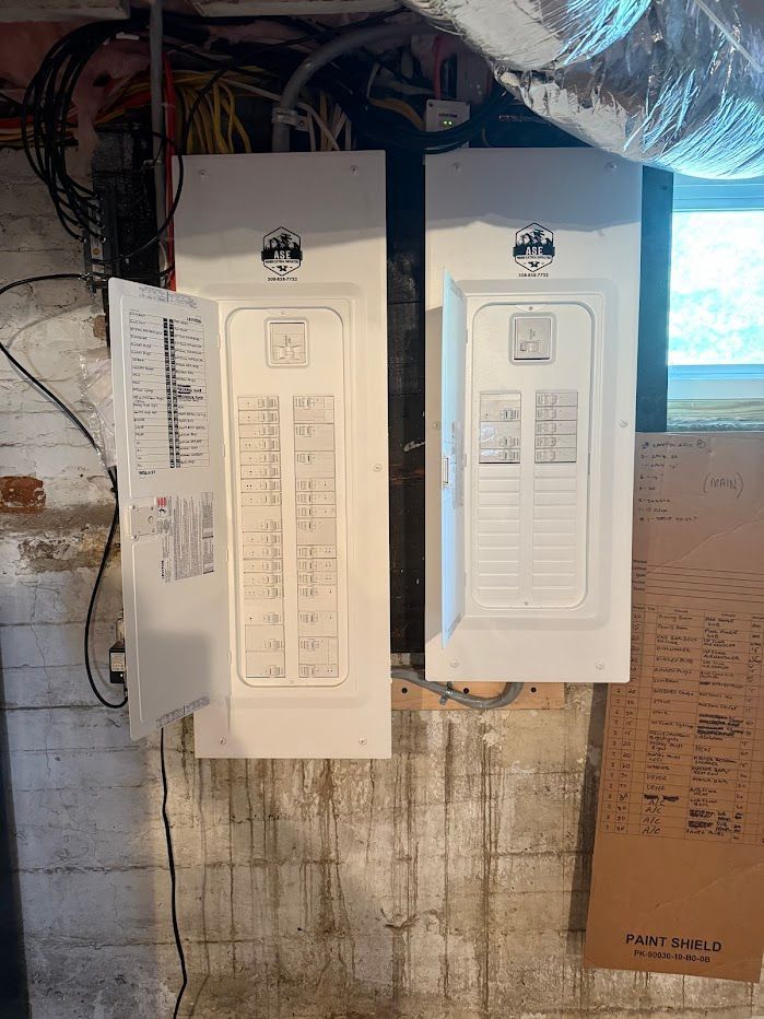Two white electrical breaker boxes on a concrete wall, one door open, in a basement.