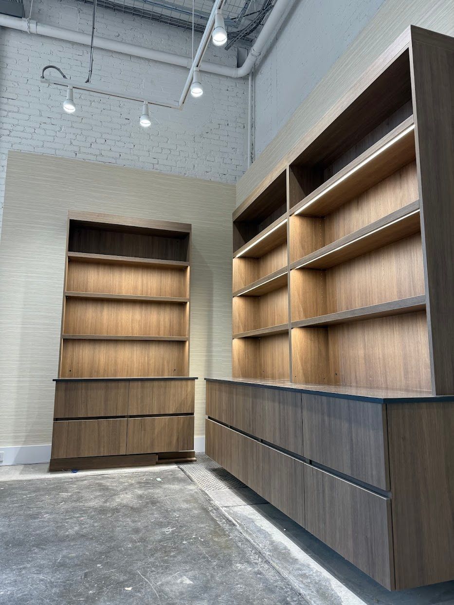 Two wooden bookshelves with drawers against a light beige wall and a concrete floor.