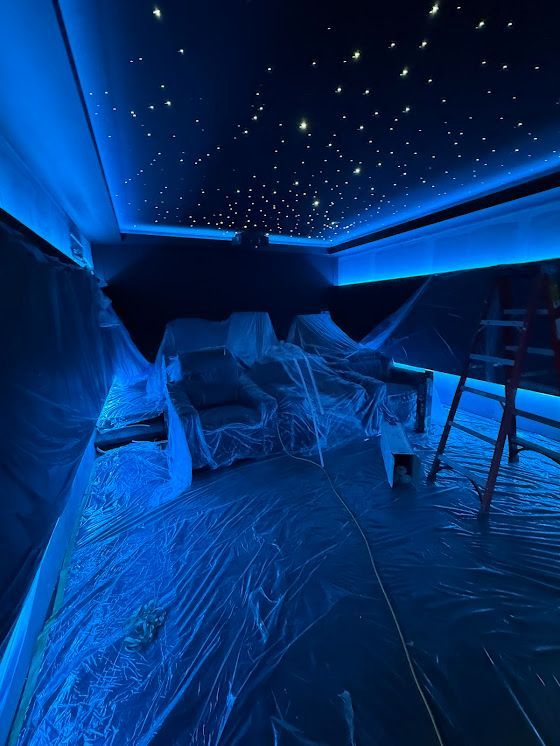 Blue-lit room with star ceiling, furniture covered in plastic, and a ladder.