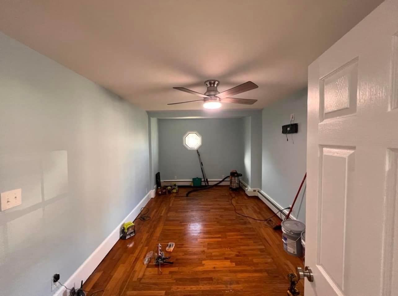 Empty room with wood floor, blue walls, ceiling fan, and open white door.