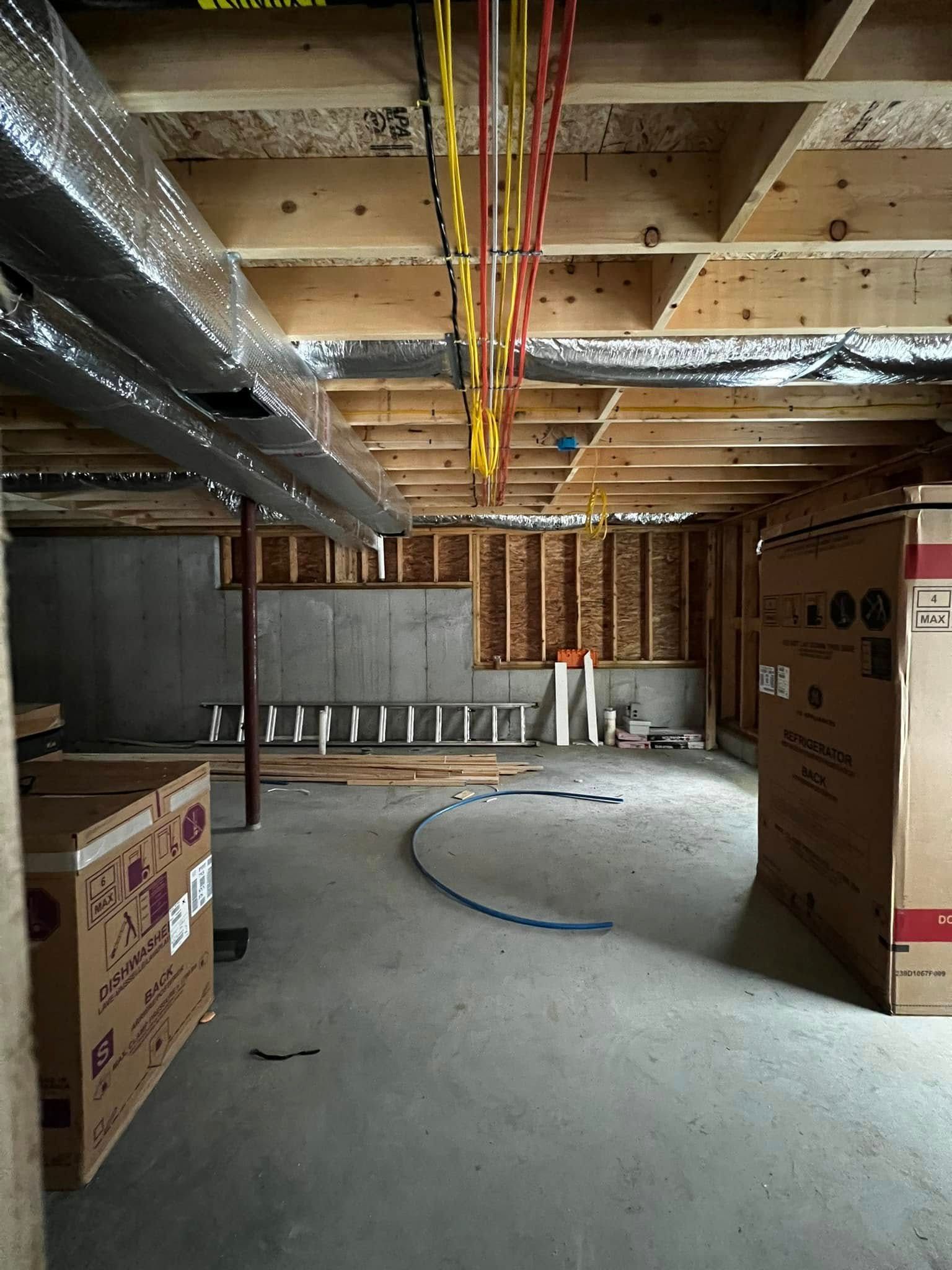 Unfinished basement with exposed beams, ductwork, and electrical wiring. Cardboard boxes line the walls.