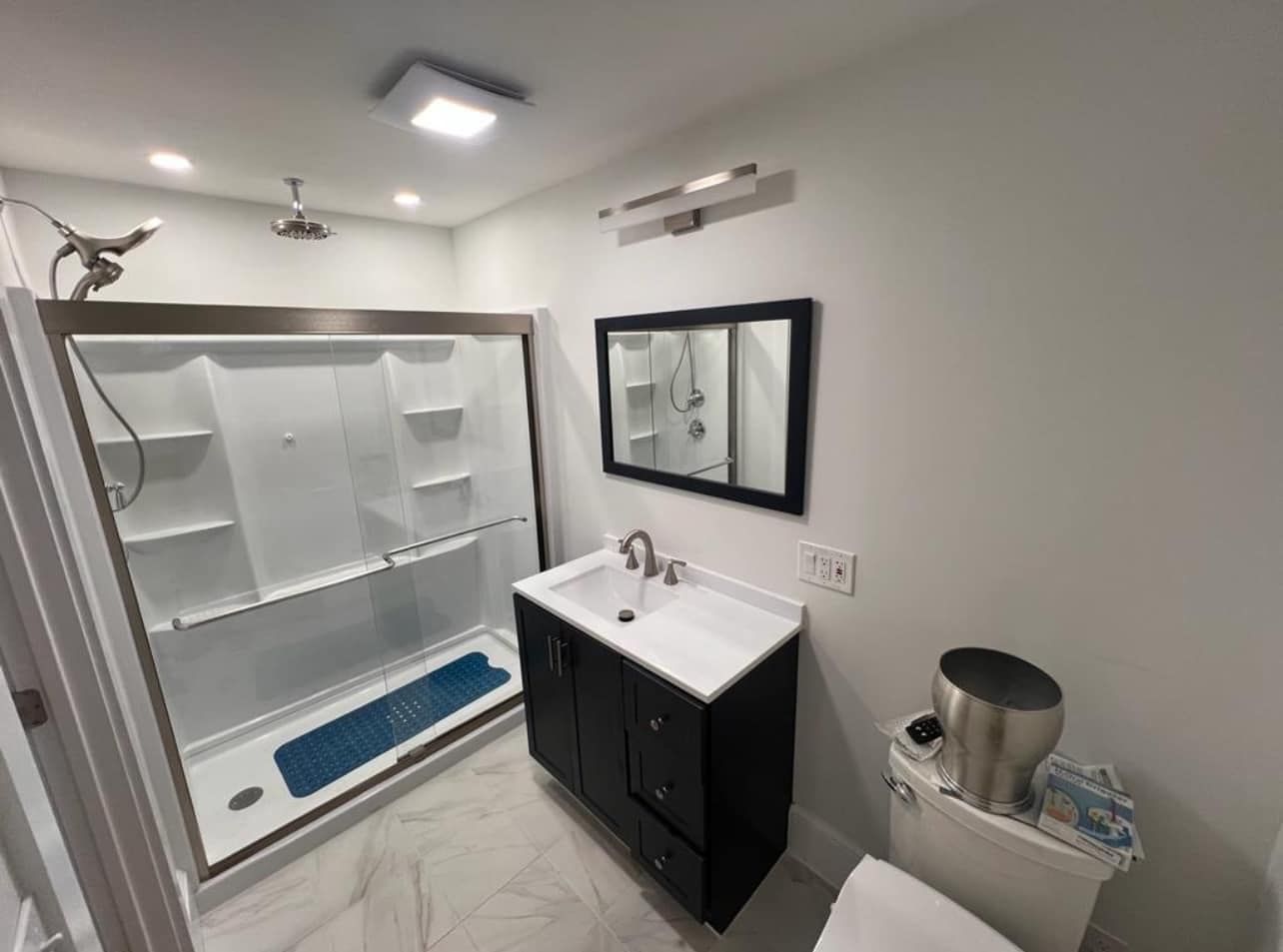 Bathroom with shower, vanity, and toilet. White walls, black vanity, silver fixtures.