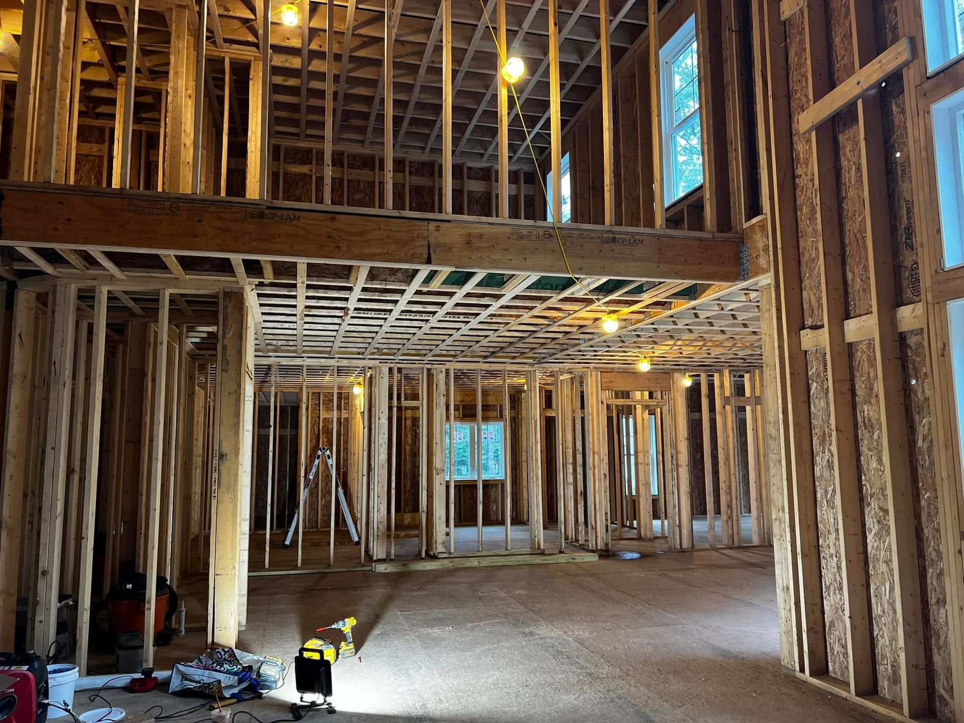 Interior of a wood-framed house under construction, showing open floors, beams, and windows.