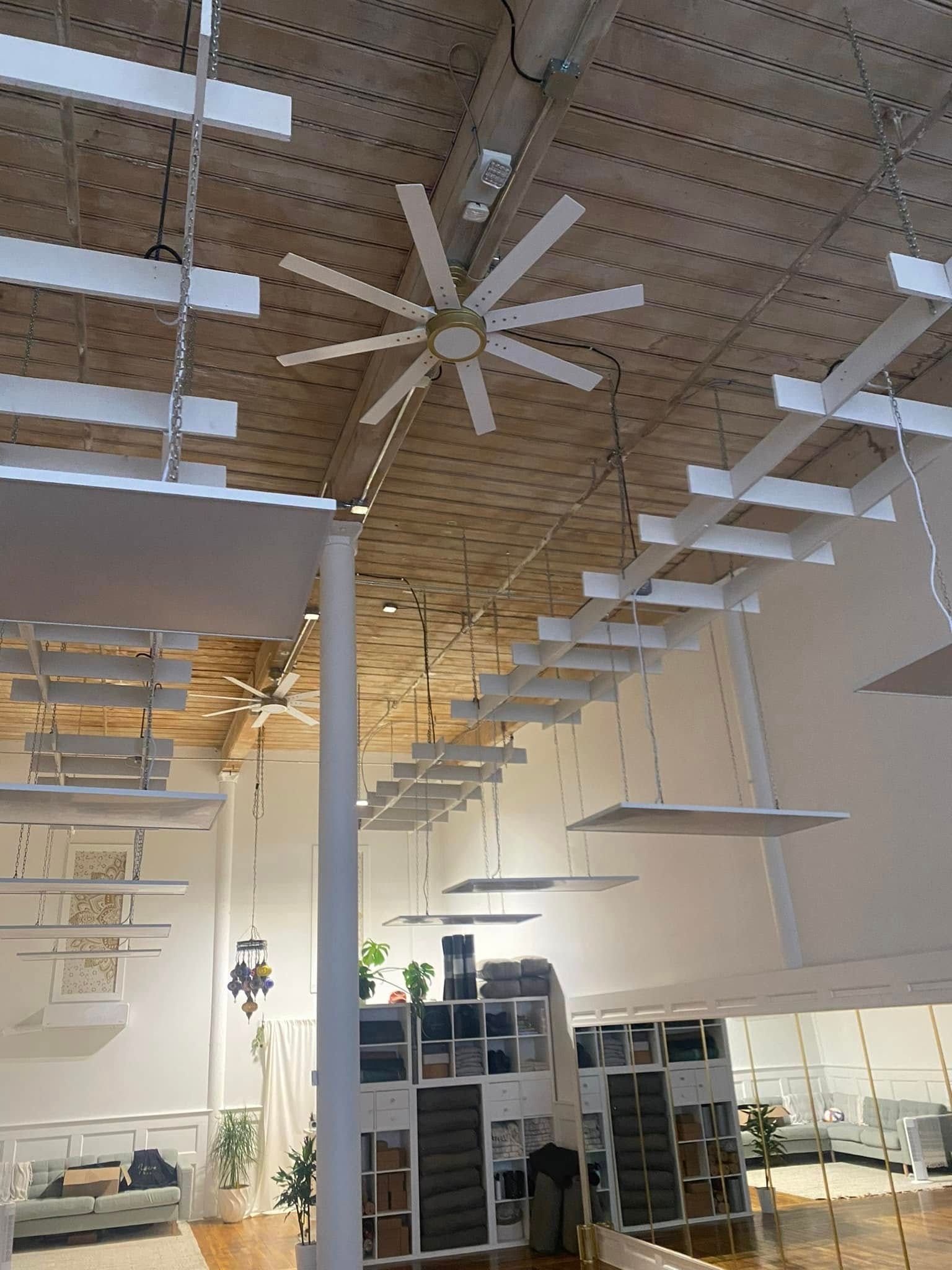 Large, high-ceilinged room with a ceiling fan and decorative slats. White shelves and furniture, wooden floor.