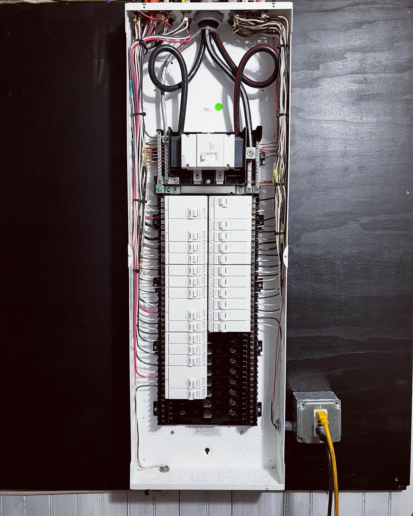 Electrical panel with wires and breakers on a black wall, Ethernet cable to the right.