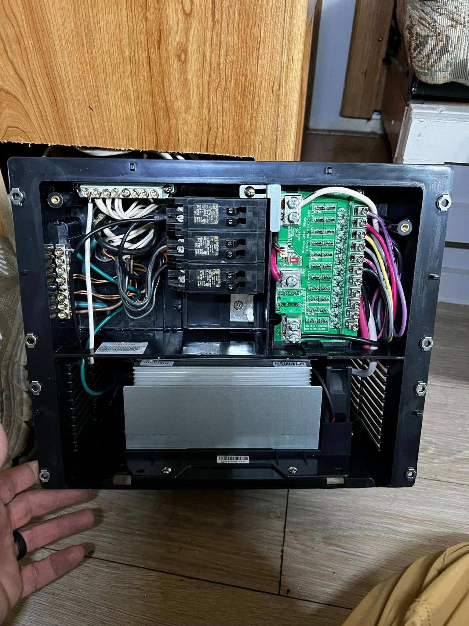 Black electrical panel with wires, circuit breakers, and a green circuit board.