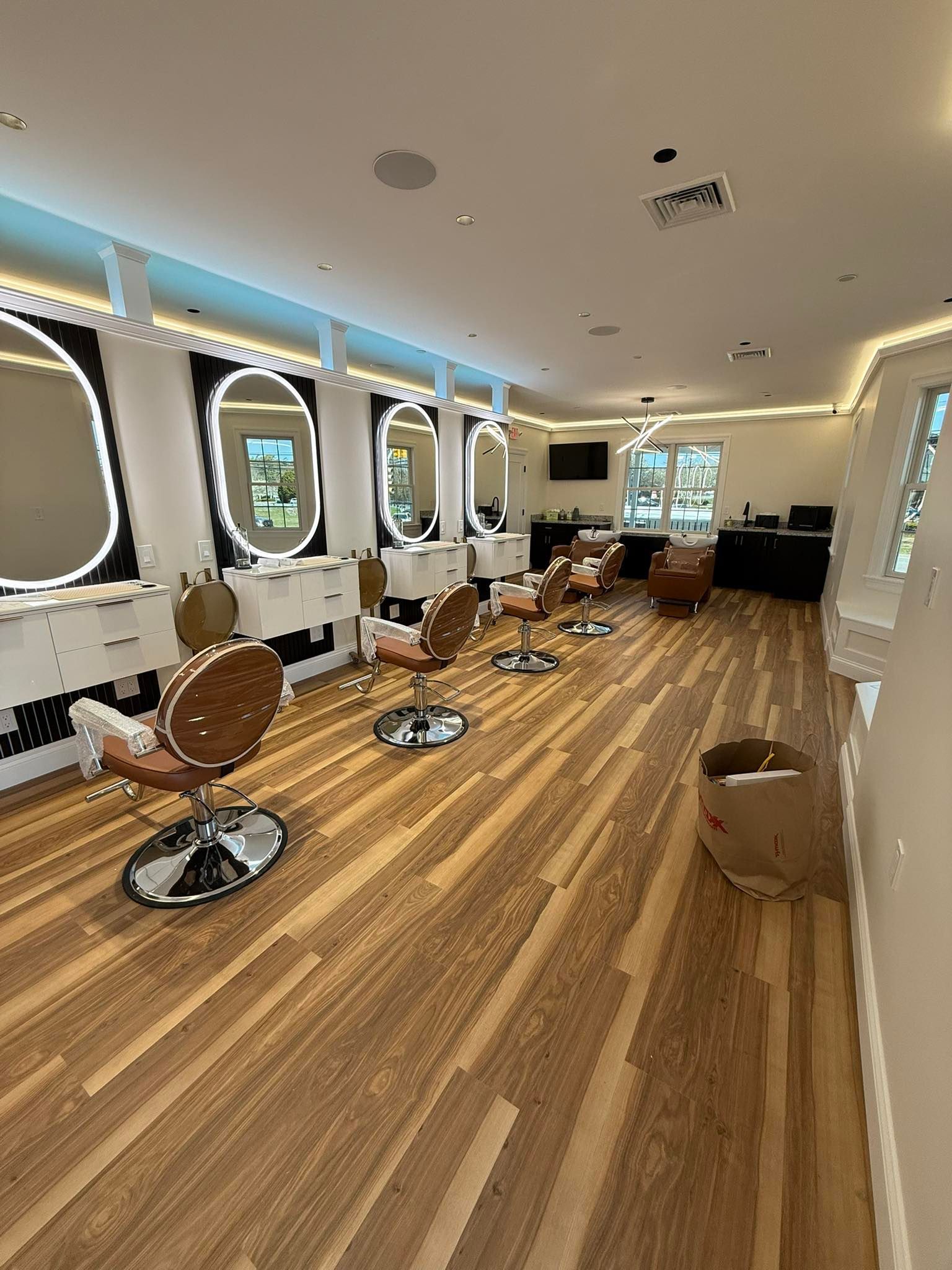 Hair salon interior with wooden floors, styling chairs, mirrors, and bright lighting.