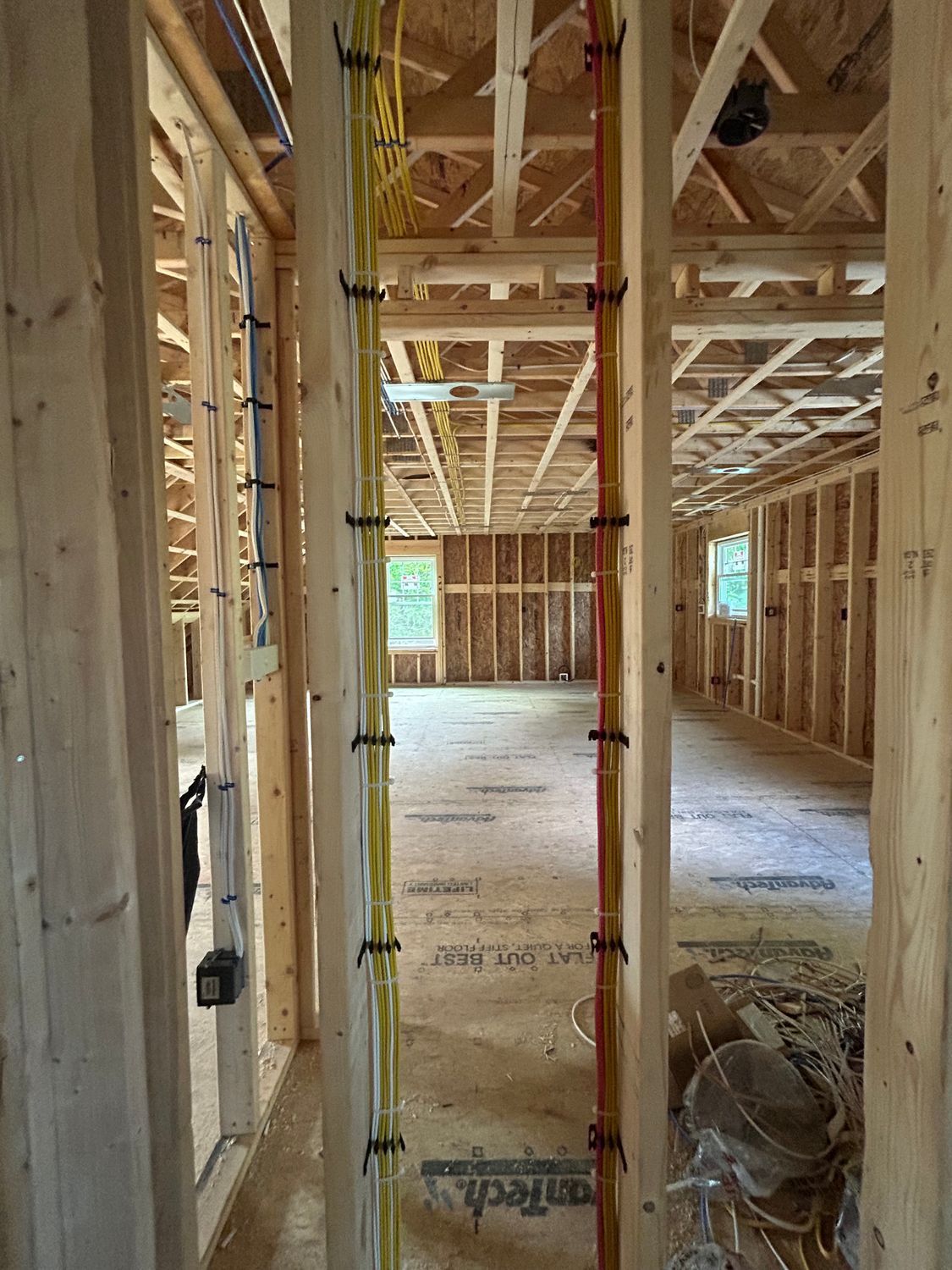 Interior of a building under construction; exposed wooden framing, electrical wires secured to the studs.