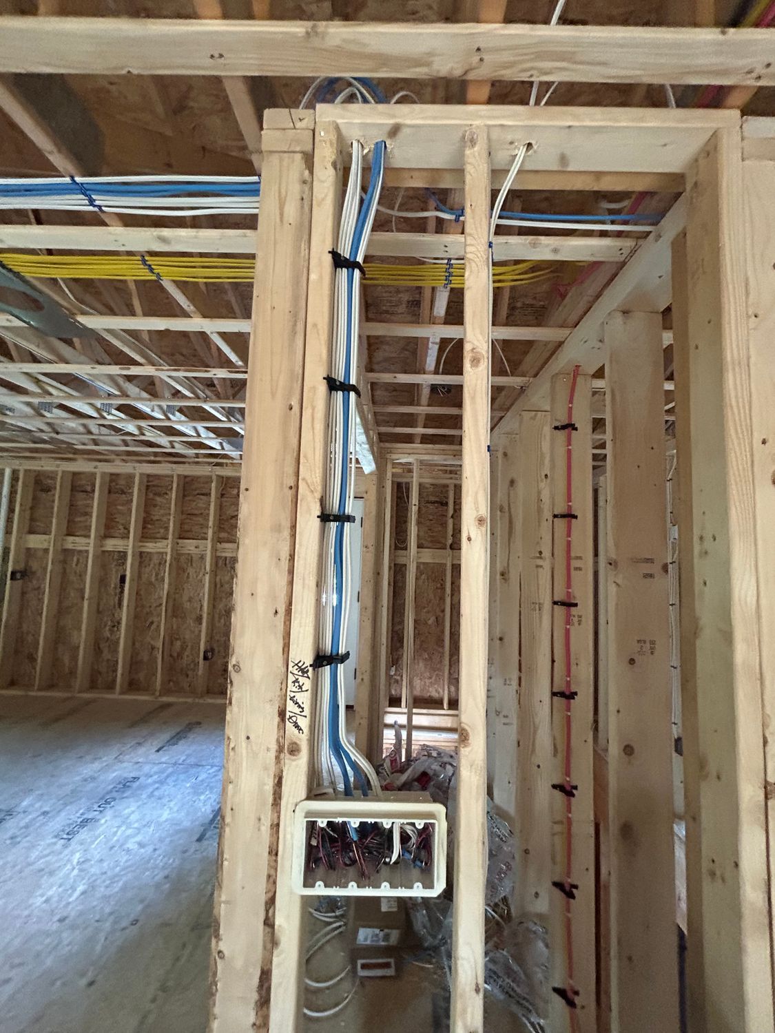 Interior view of a building under construction, showing bundled wires, electrical boxes, and wooden framing.