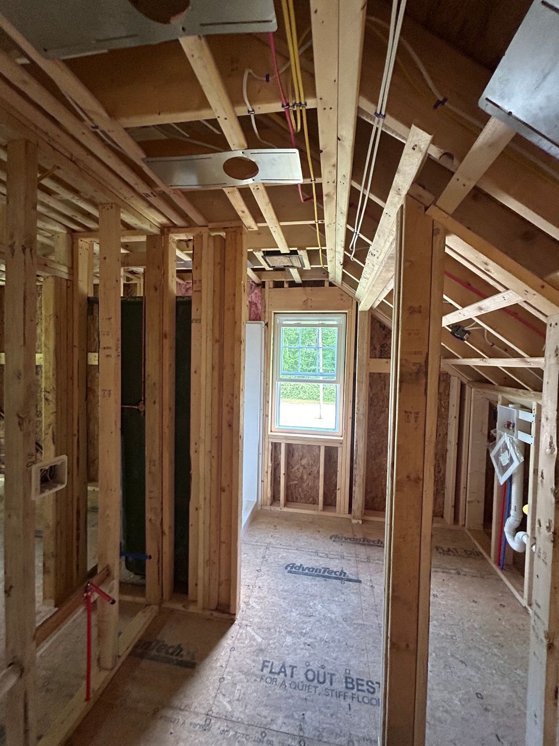 Interior of a room under construction, with exposed wooden framing, a window, and electrical wiring.