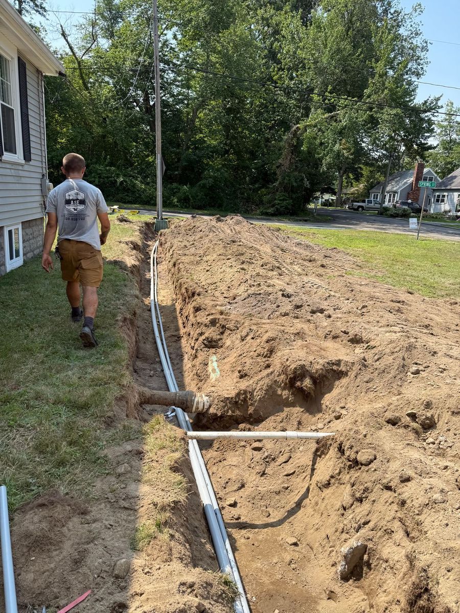 Man walking near a trench with buried electrical conduit. Sunny day, residential setting.
