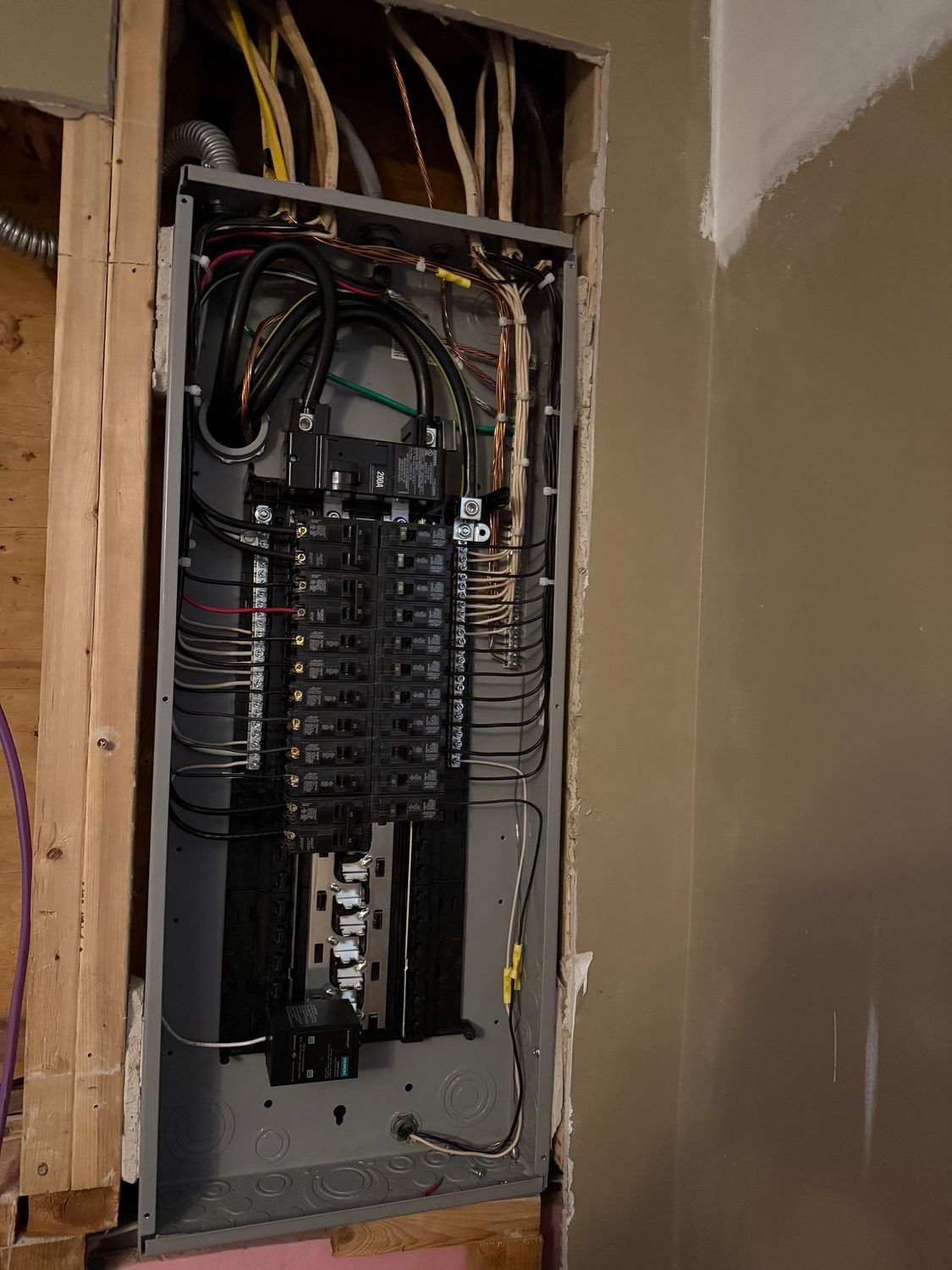 Electrical panel installed in a wall, with wires and circuit breakers visible.