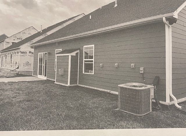 A black and white photo of a house with a air conditioner in the backyard.