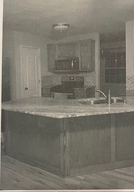 A black and white photo of a kitchen with a sink , stove and microwave.