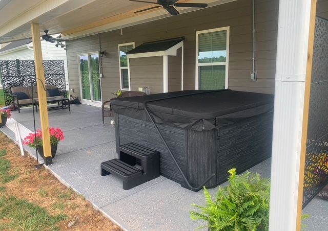 A hot tub is sitting on a covered patio next to a house.