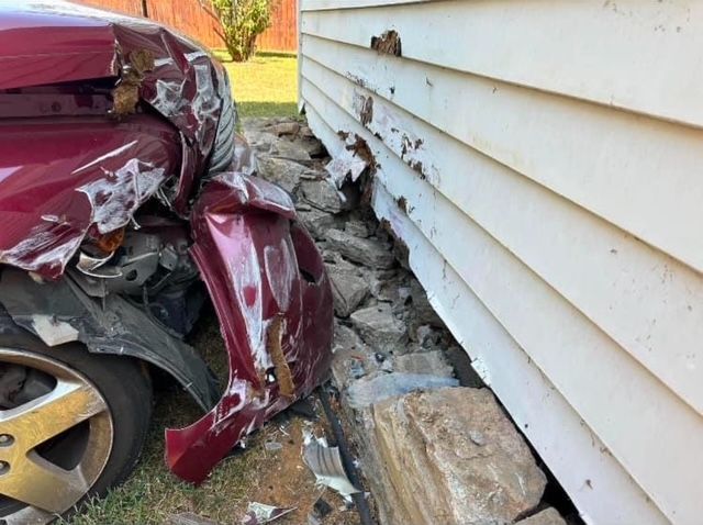 A red car has crashed into a white house.
