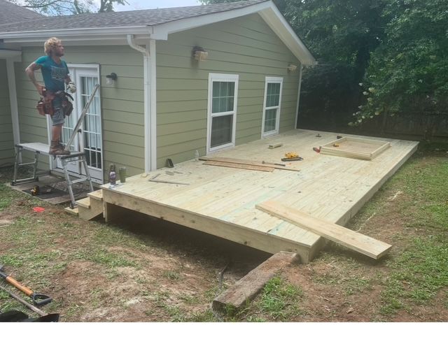 A man is standing on a ladder next to a wooden deck in front of a house.