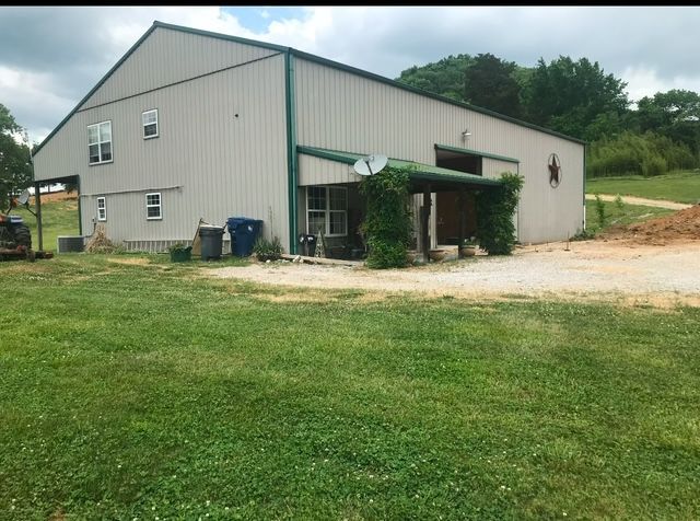 A large white building with a green roof is sitting in the middle of a grassy field.