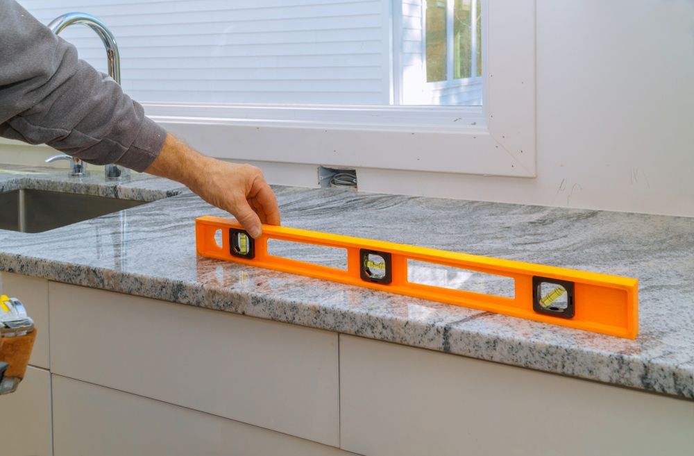 A person is measuring a granite counter top with an orange level.