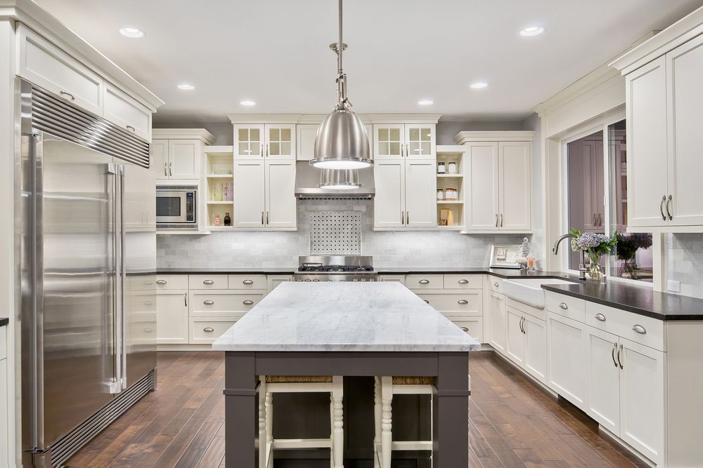 A kitchen with white cabinets , stainless steel appliances , and a large island.