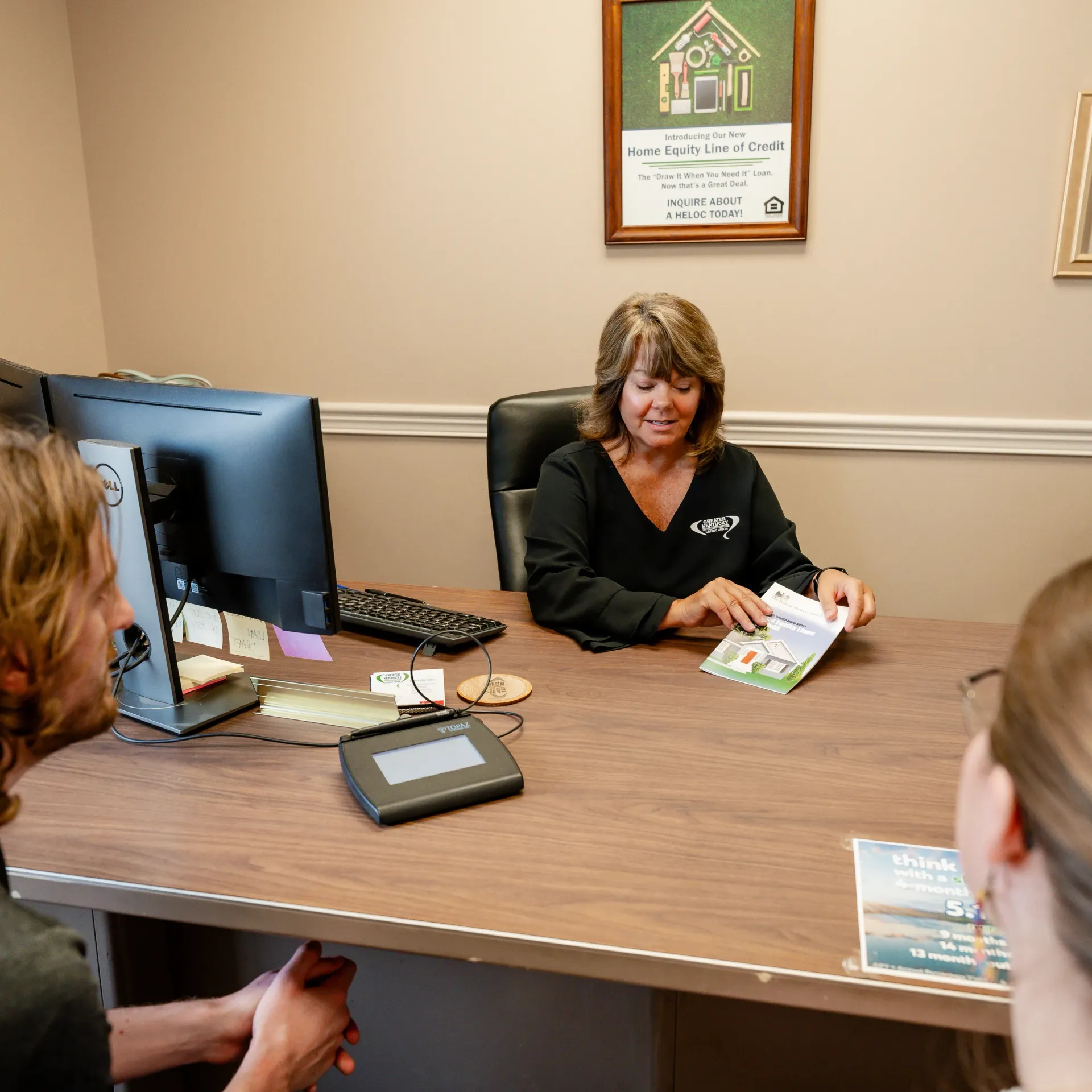 Woman at desk showing documents to two people. Office setting.