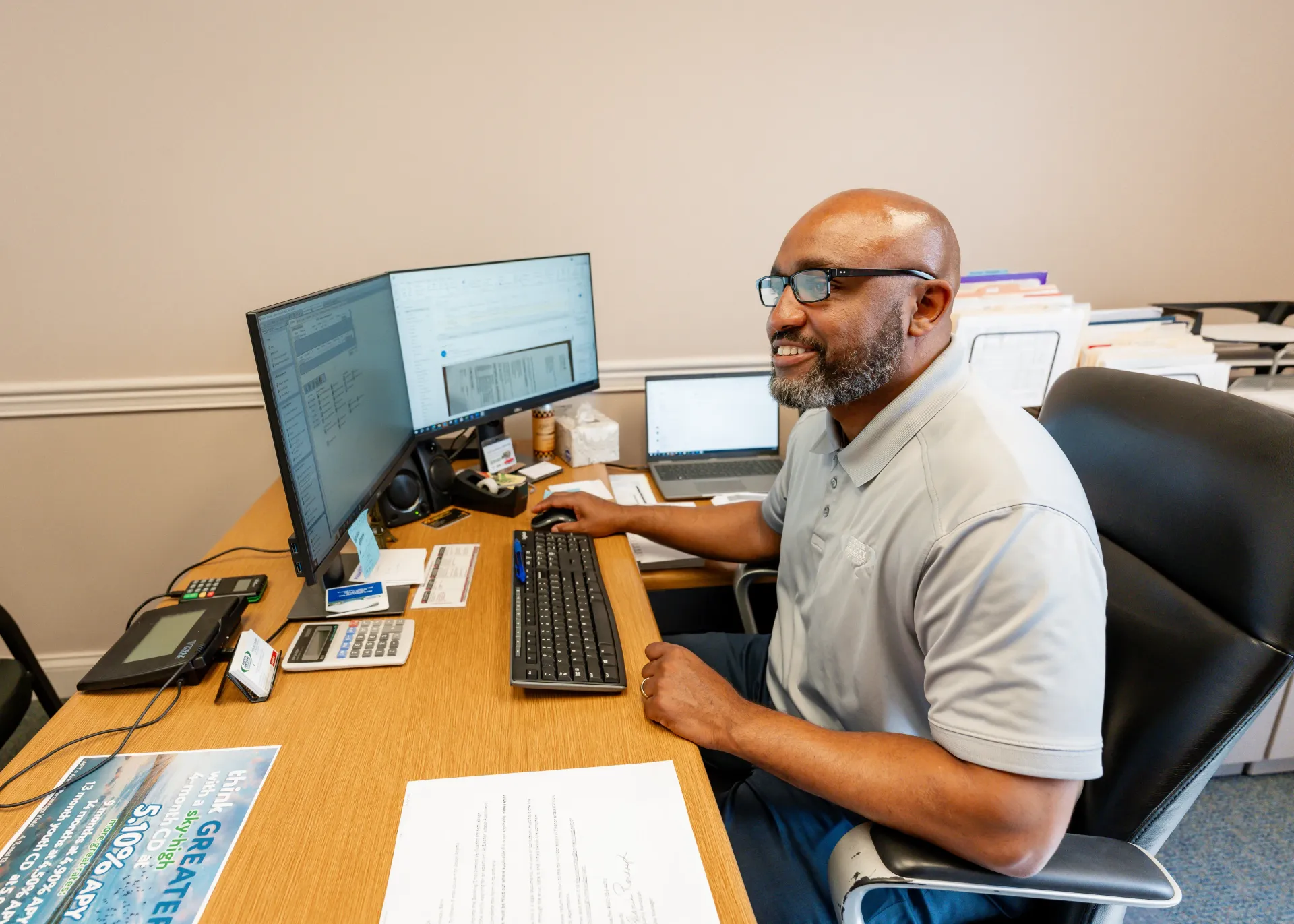 Man at desk with two monitors and laptop, working with a keyboard and mouse.