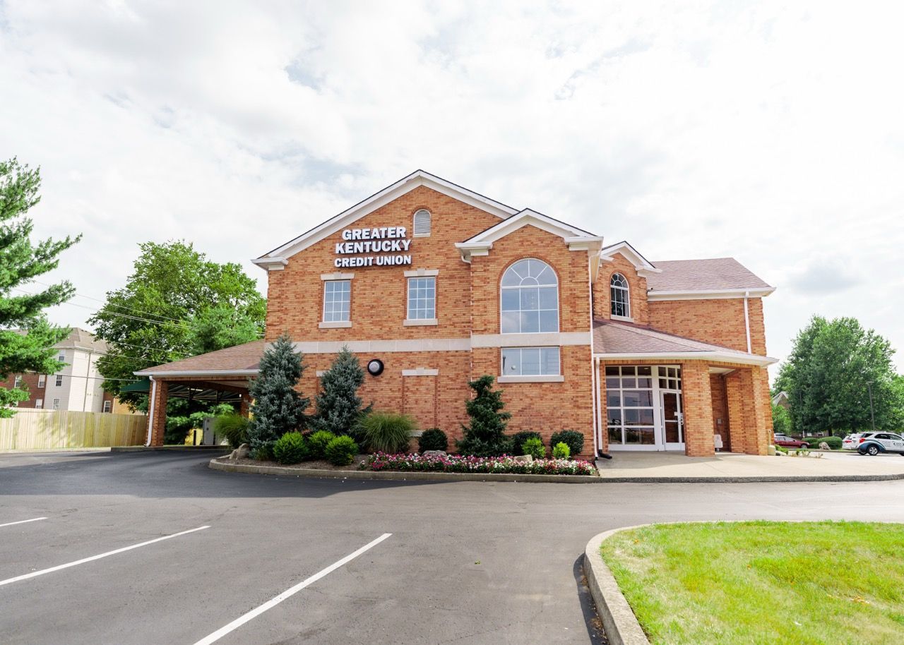 Brick building with arched window and sign, surrounded by parking lot and landscaping.