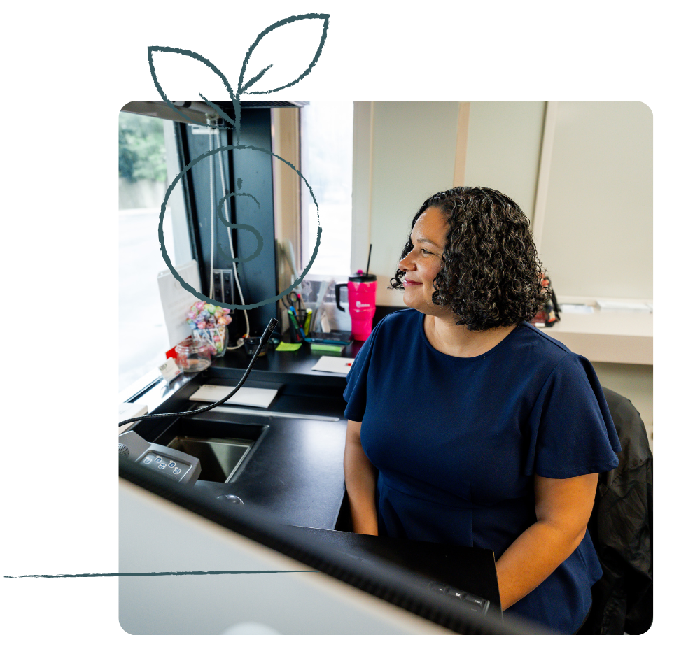 Woman in blue top seated at a desk, smiling and looking to the side. Office setting.
