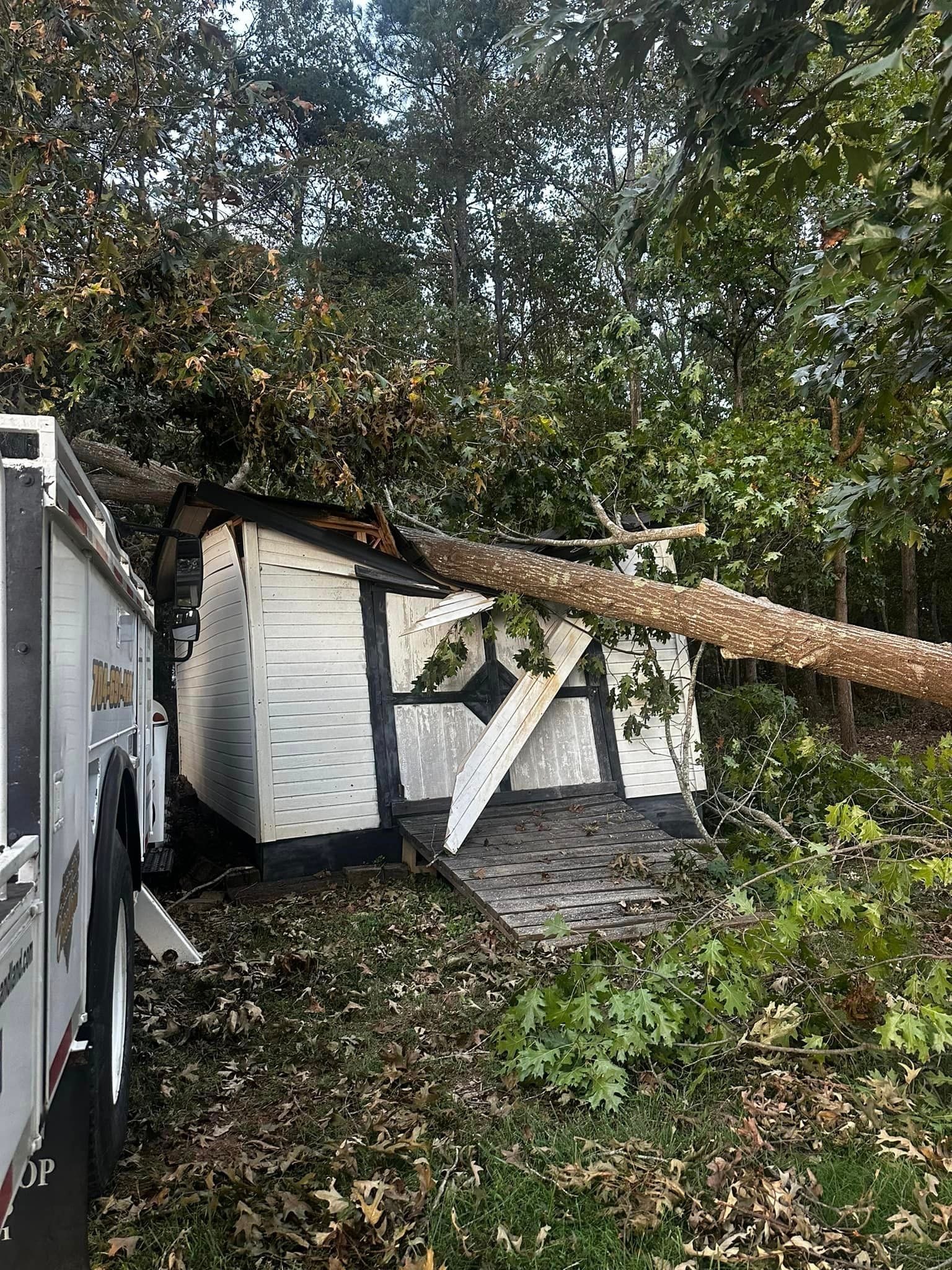 A tree fallen on a white shed with black trim; emergency vehicle on the left.