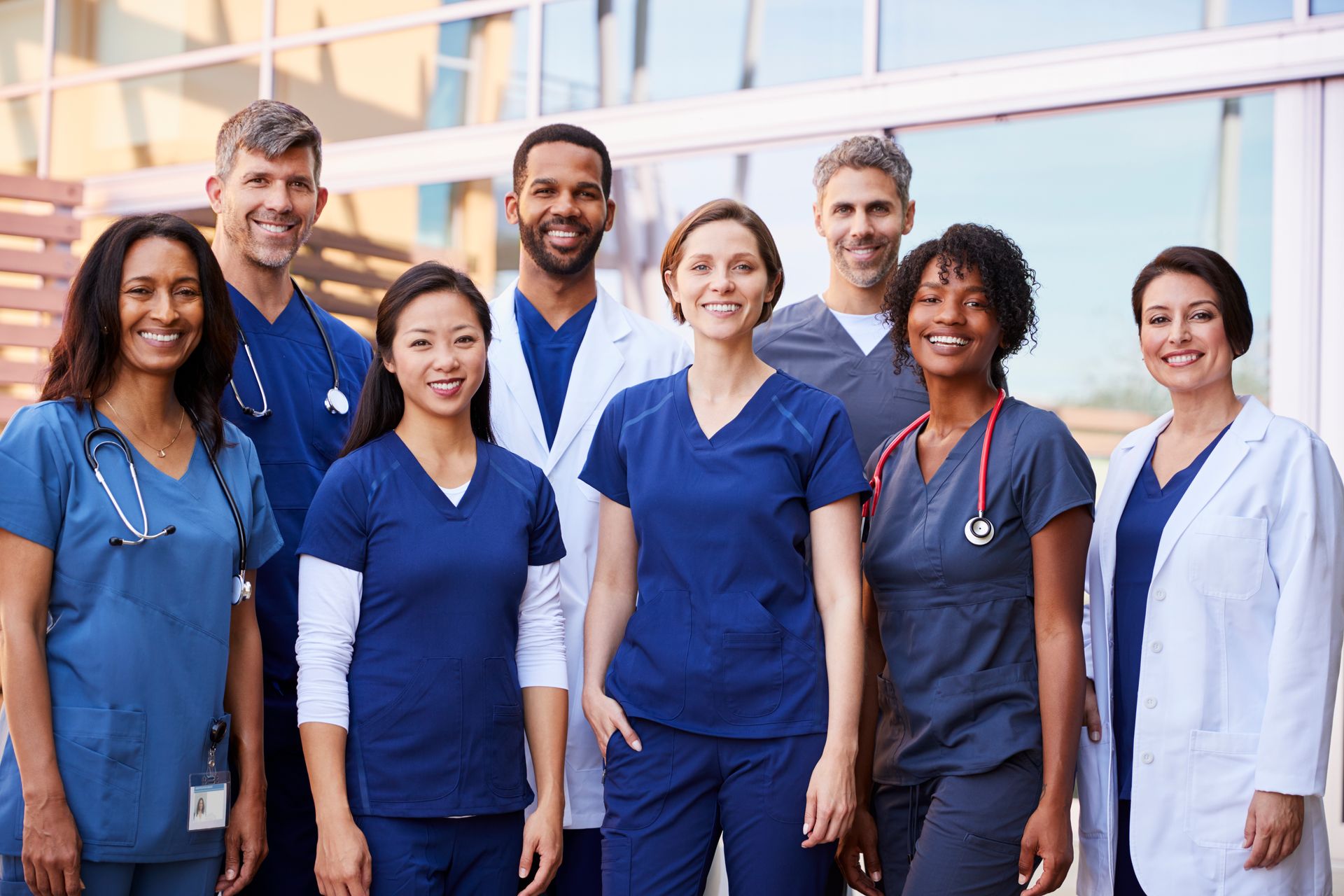 A group of doctors and nurses are posing for a picture in front of a hospital building.