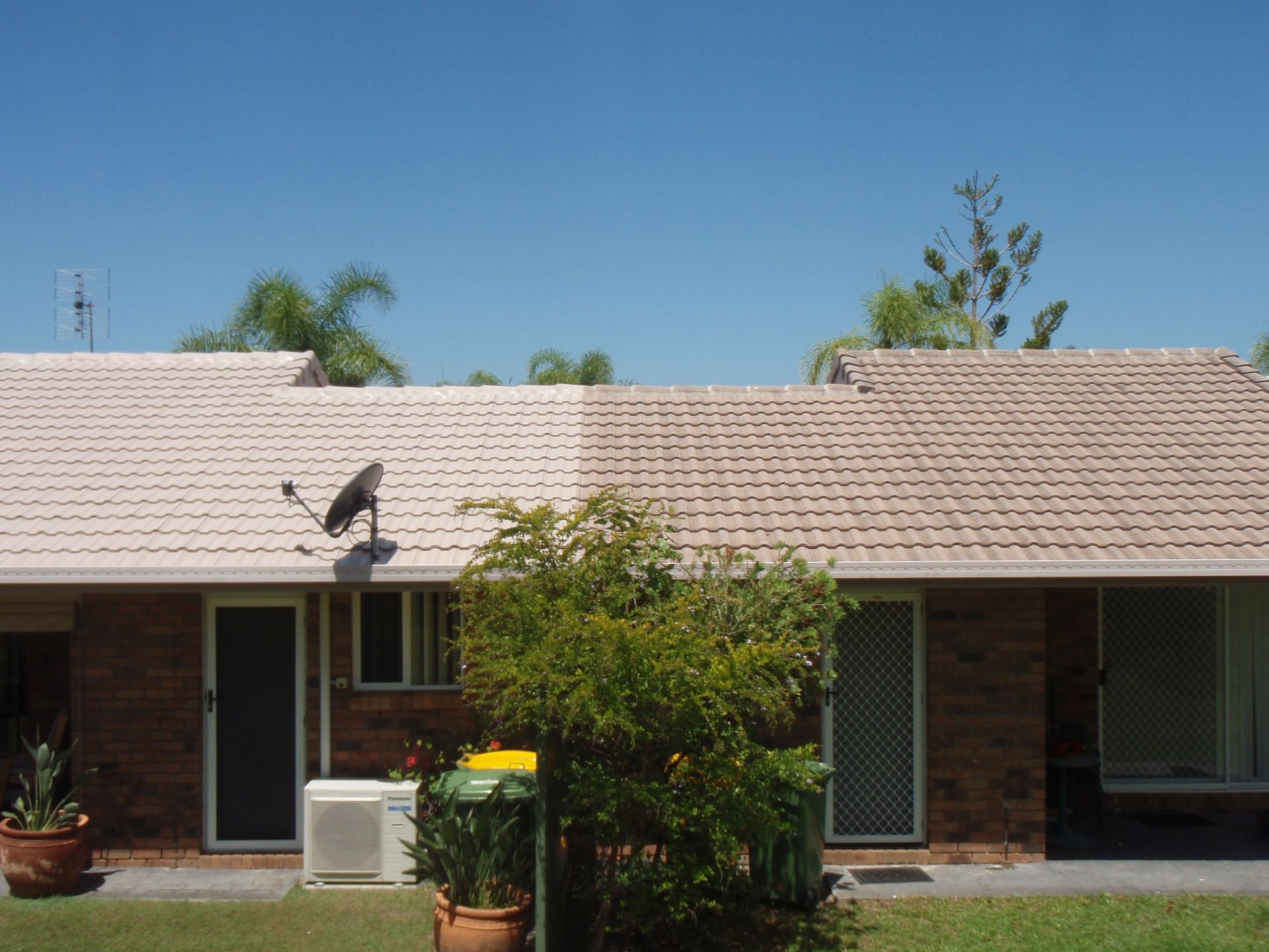 A Man Is Cleaning The Roof Of A House With A High Pressure Washer — Gold Coast Roof Repairs in Mudgeeraba, QLD