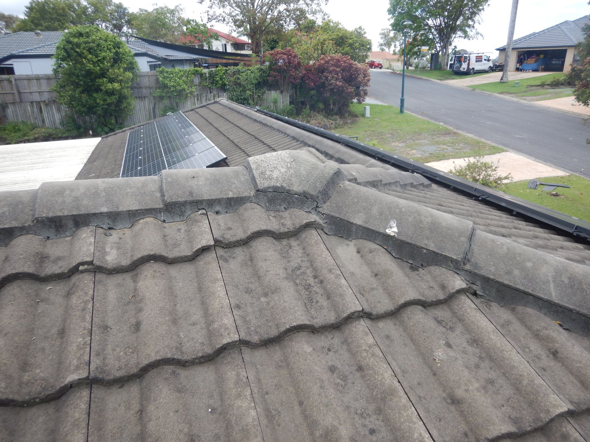 A Man In A Yellow Hard Hat Is Looking At A Roof — Gold Coast Roof Repairs in Mudgeeraba, QLD