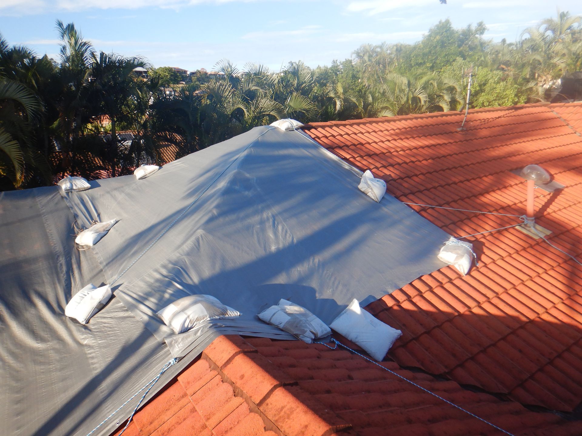 A Man In A Red Shirt Is Standing On Top Of A Tiled Roof — Gold Coast Roof Repairs in Oxenford, QLD