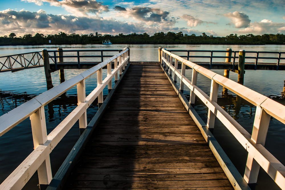 A Wooden Dock Leading To A Body Of Water With A White Railing — Gold Coast Roof Repairs in Tweed Heads, NSW