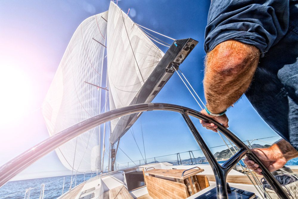 A Man Is Steering A Sailboat In The Ocean — SRG Automotive and Marine in Aitkenvale, QLD