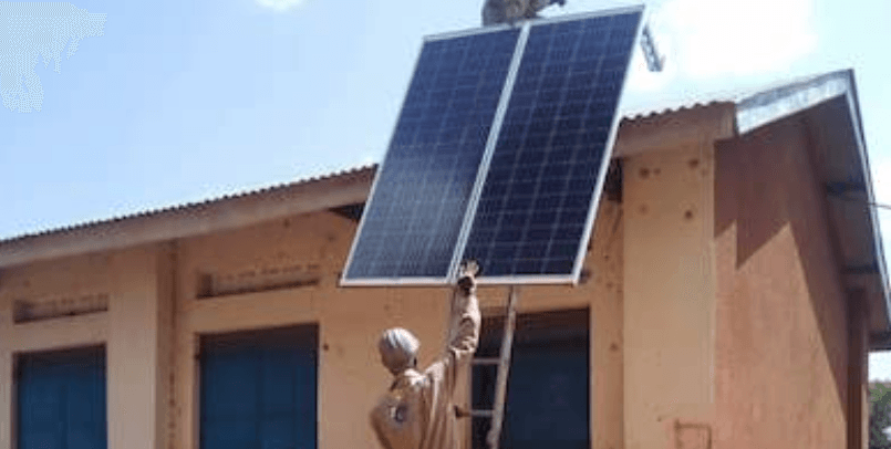 A man is standing on a ladder holding a solar panel on top of a building.