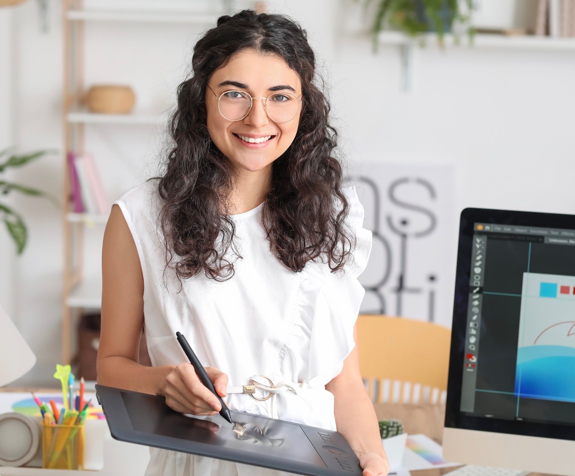 A woman is holding a pen and a tablet in front of a computer.