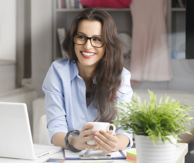 A woman is sitting at a desk with a laptop and a cup of coffee.