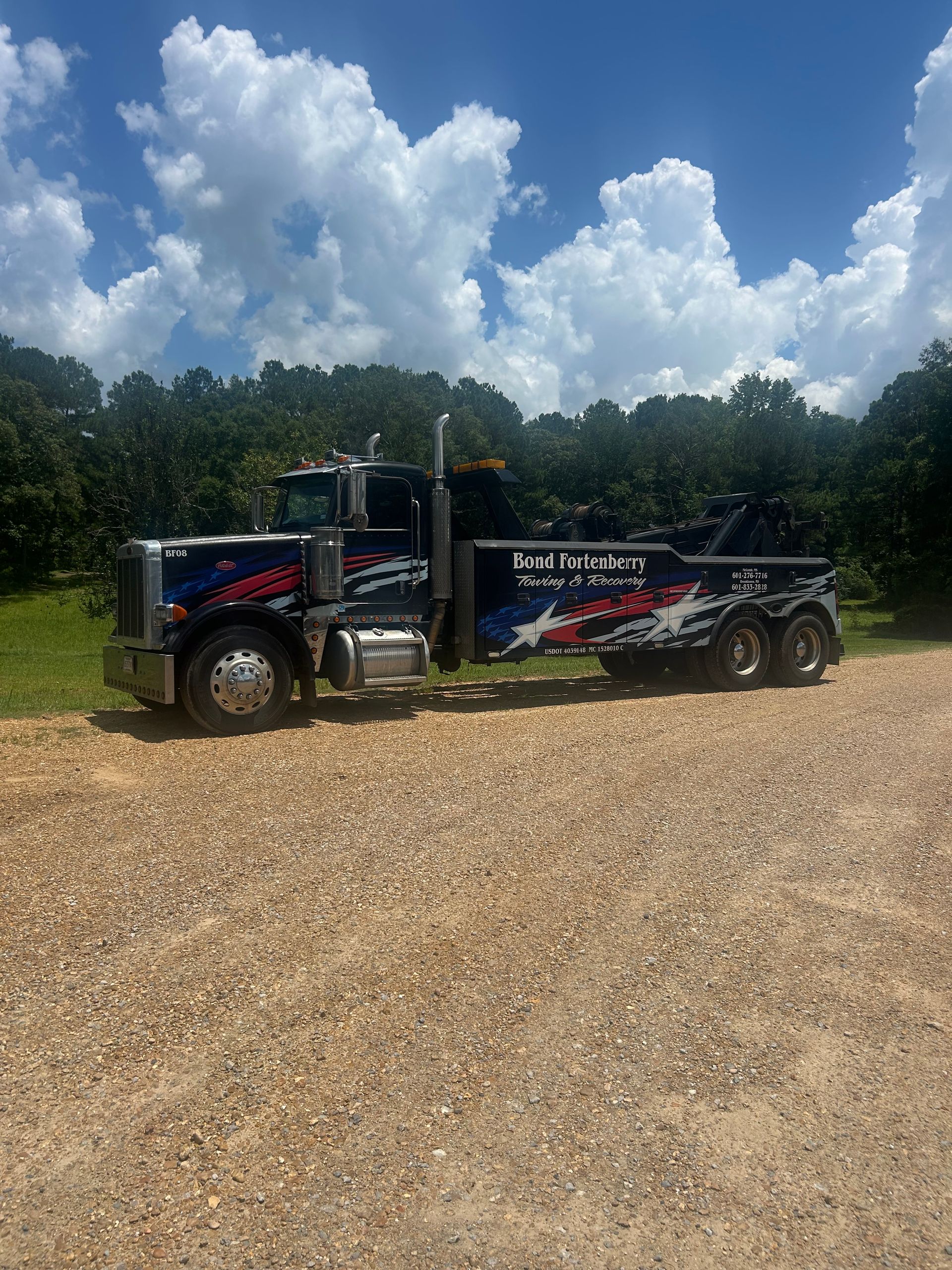 A large tow truck is parked on a gravel road.