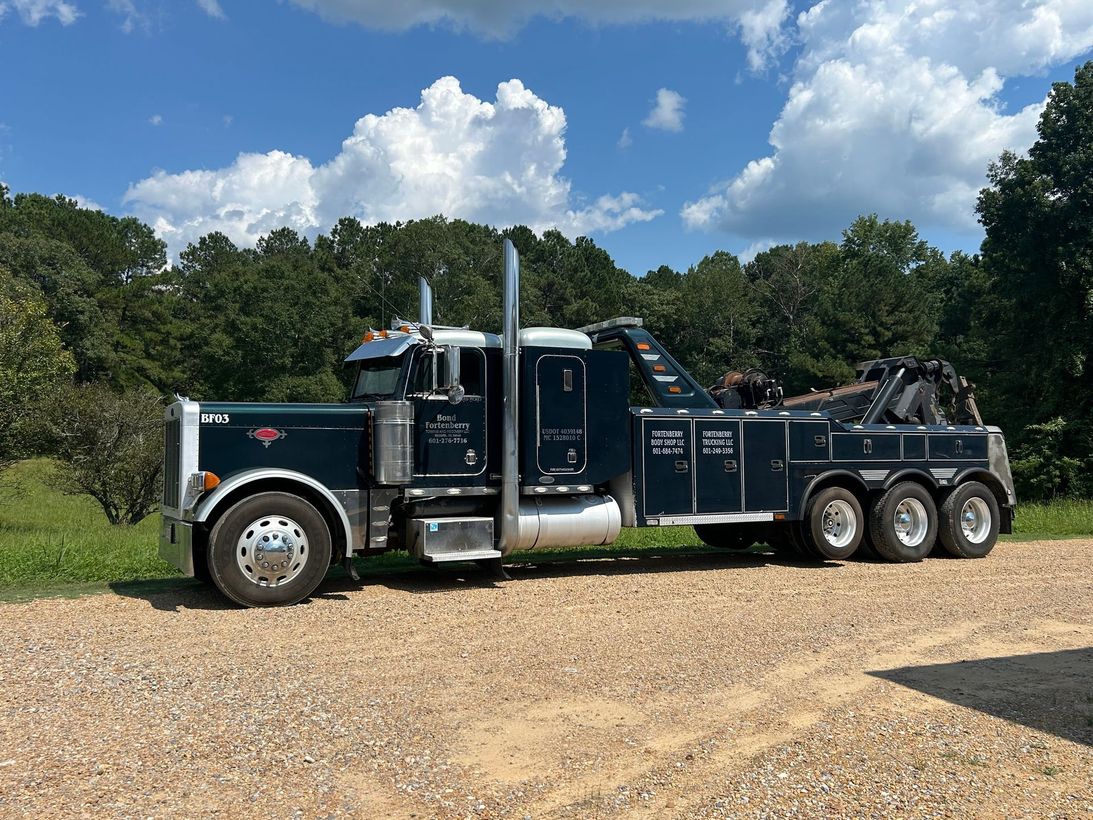 A large tow truck is parked on a gravel road.