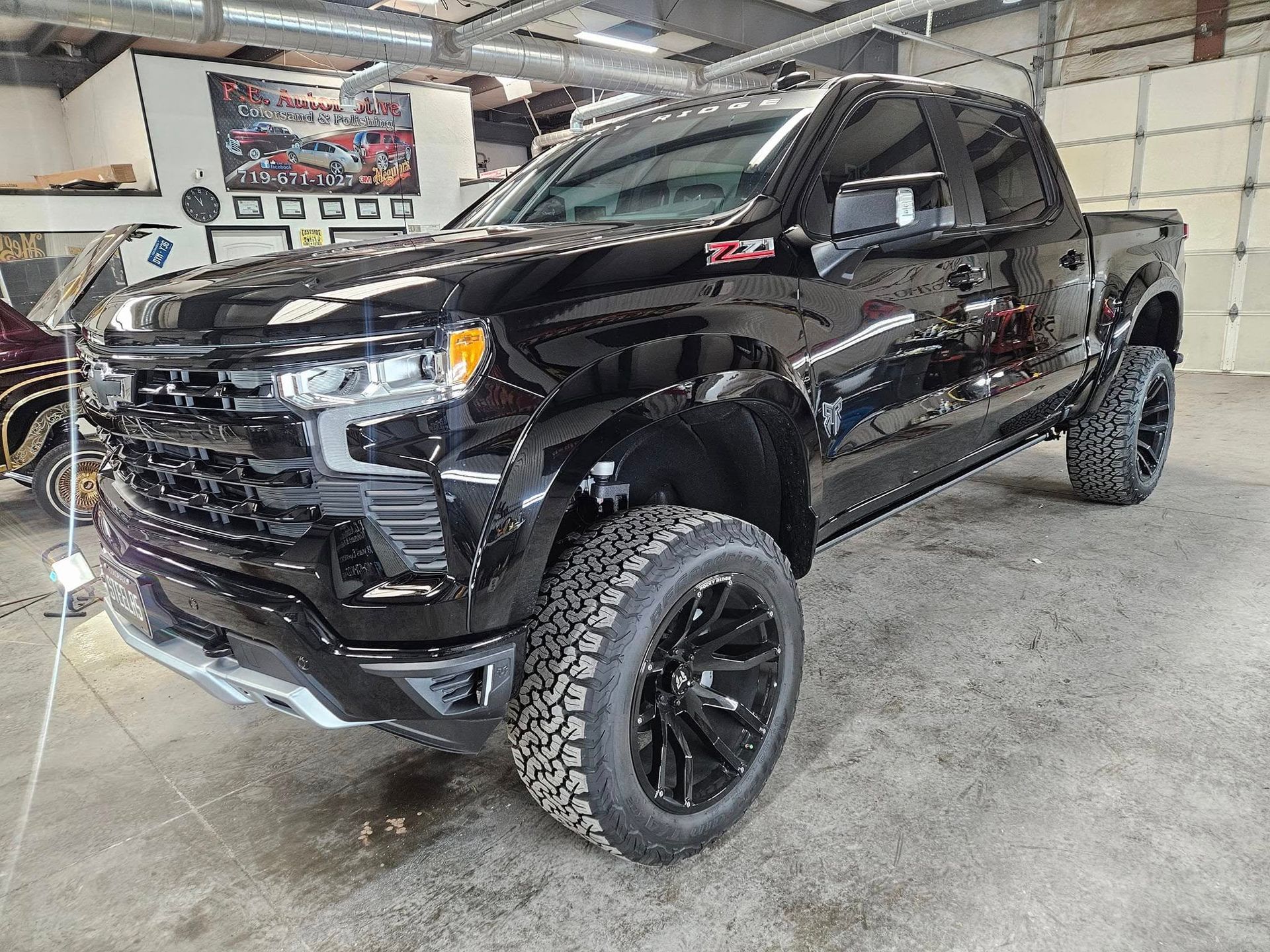 Black Chevrolet Silverado pickup truck with large off-road tires, parked inside a garage.