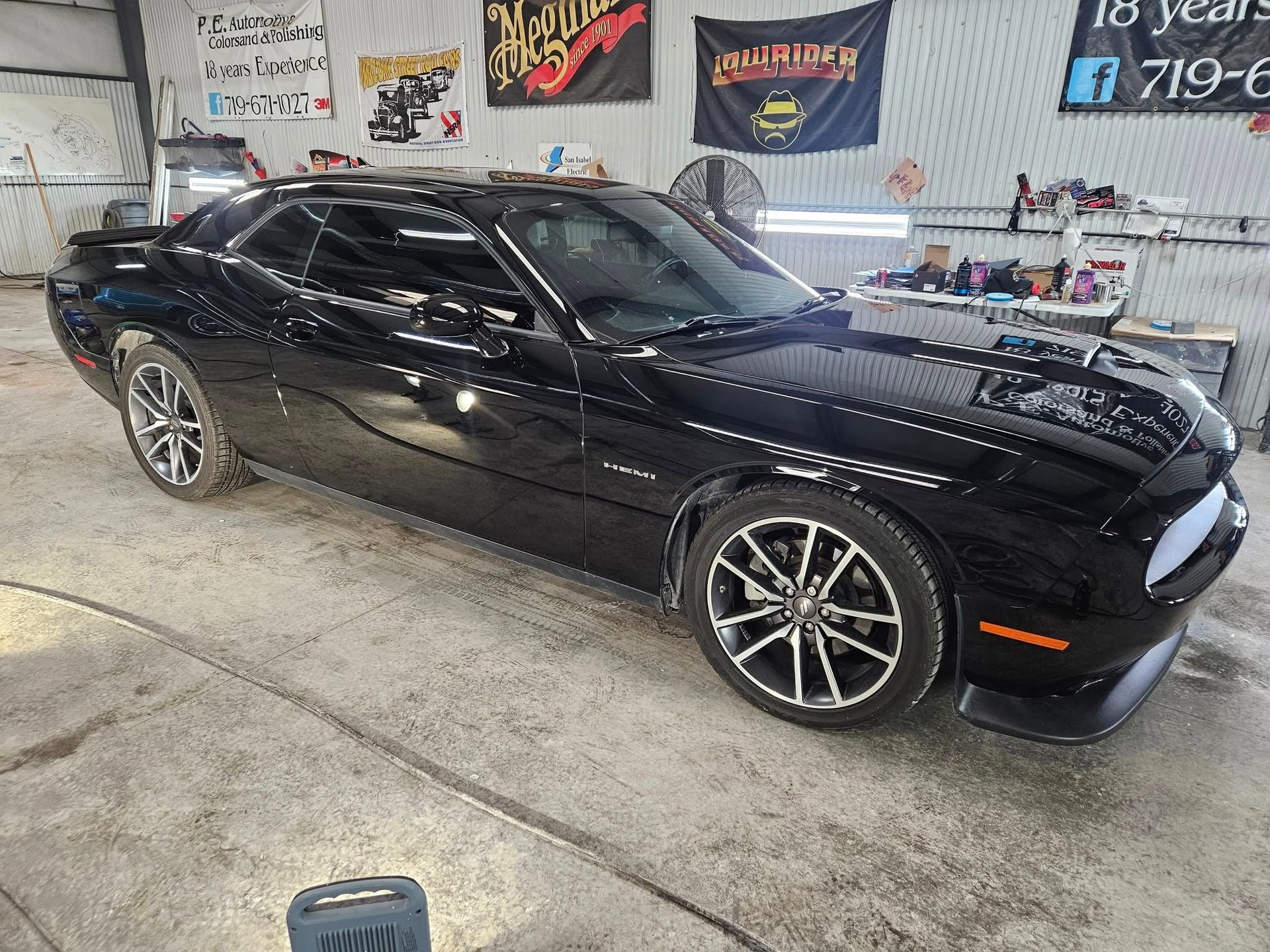 Black Dodge Challenger parked inside a garage, next to detail equipment.
