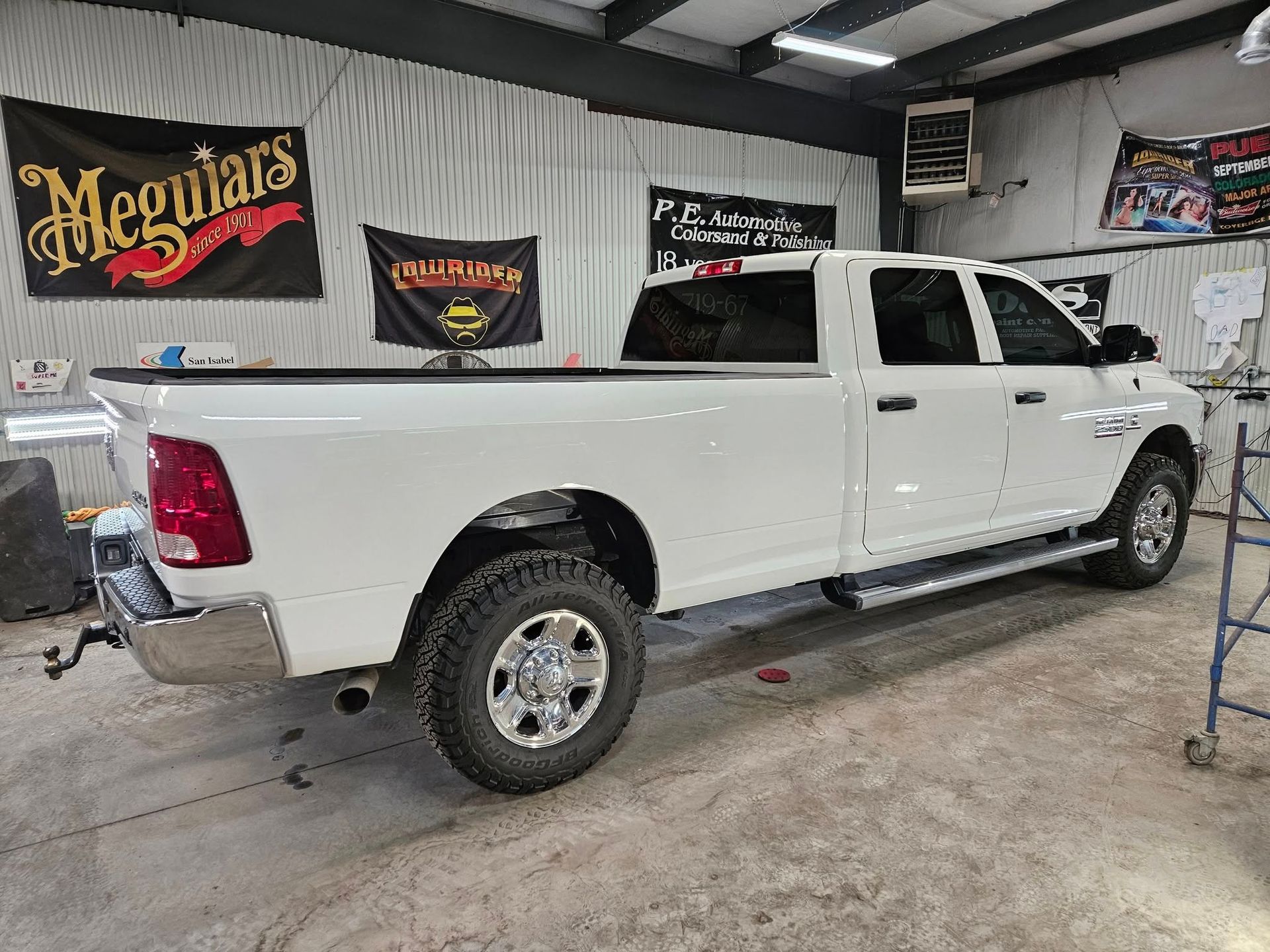 White Dodge Ram pickup truck in a garage, with Meguiar's and other flags on the wall.