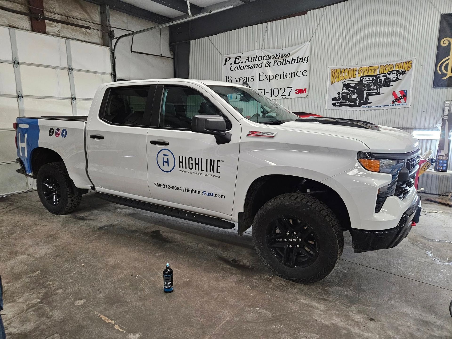 White Highline truck with black wheels in a garage setting with business branding.