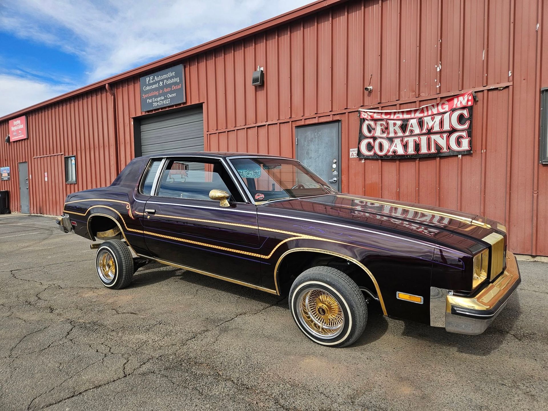 Lowrider car with gold accents parked outside a building with a ceramic coating sign.