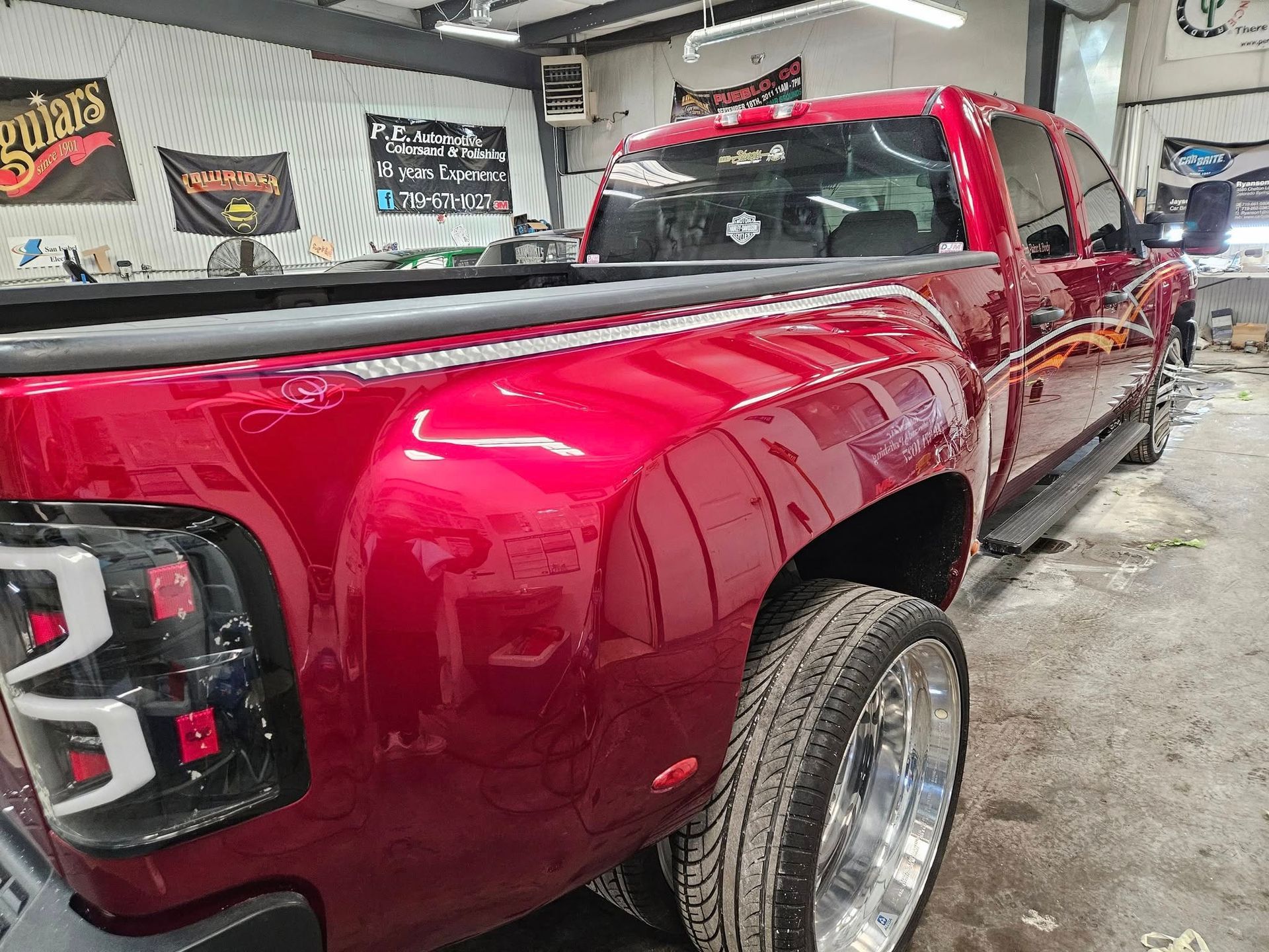 Red pickup truck with shiny paint, large chrome wheels, and custom taillights in a garage.
