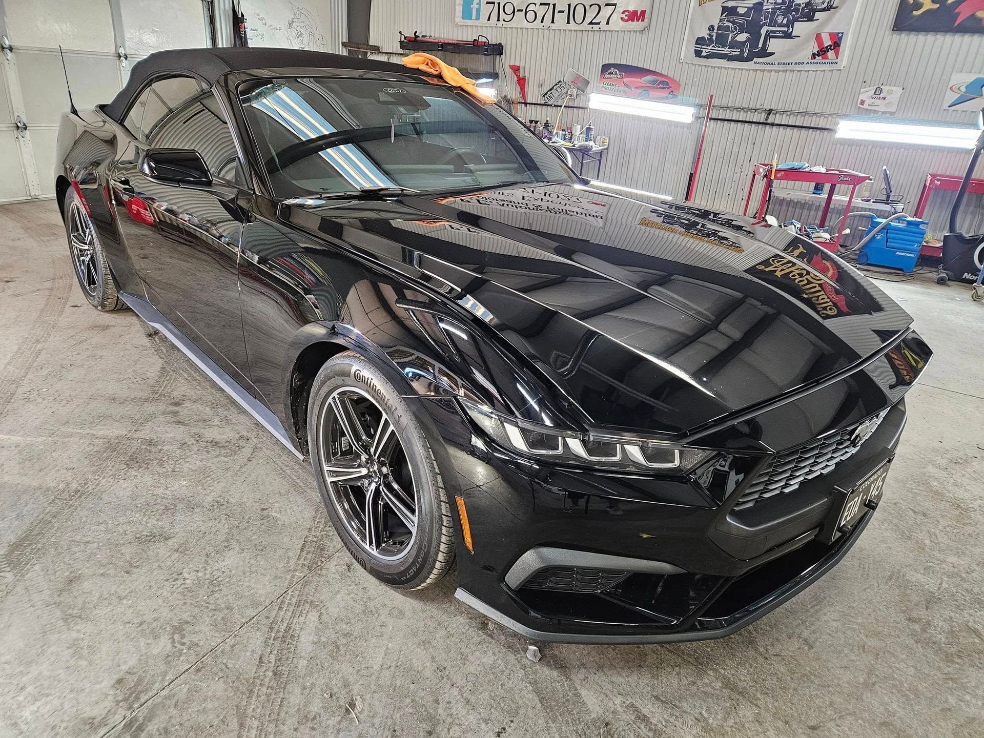 Black convertible Mustang in a garage, shiny, well-lit.